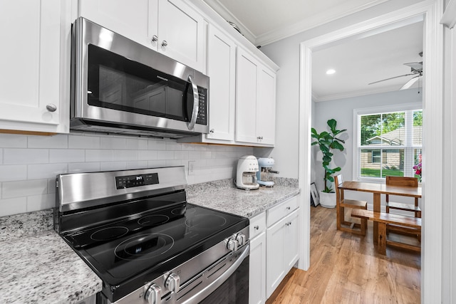 kitchen with appliances with stainless steel finishes, white cabinets, light stone countertops, light wood-type flooring, and crown molding