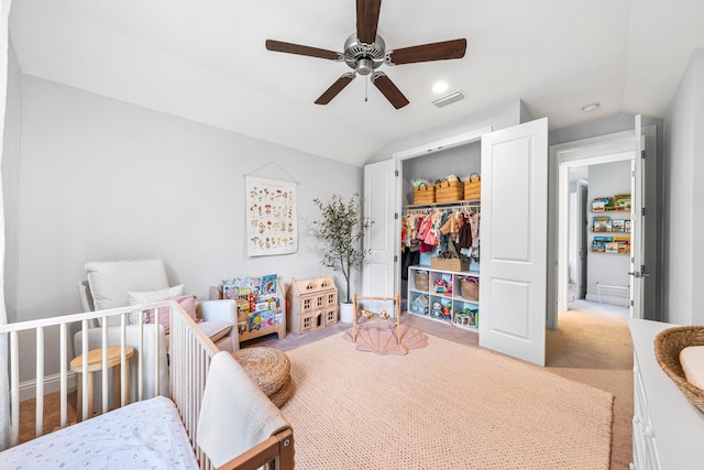 bedroom featuring vaulted ceiling, a nursery area, a closet, ceiling fan, and light colored carpet