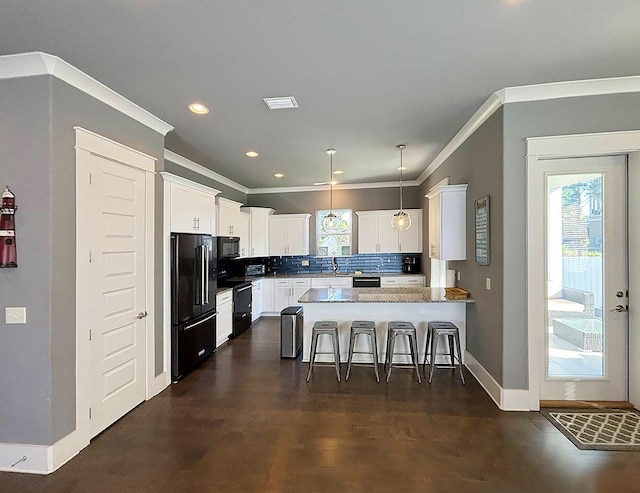 kitchen featuring hanging light fixtures, tasteful backsplash, white cabinetry, black appliances, and a breakfast bar