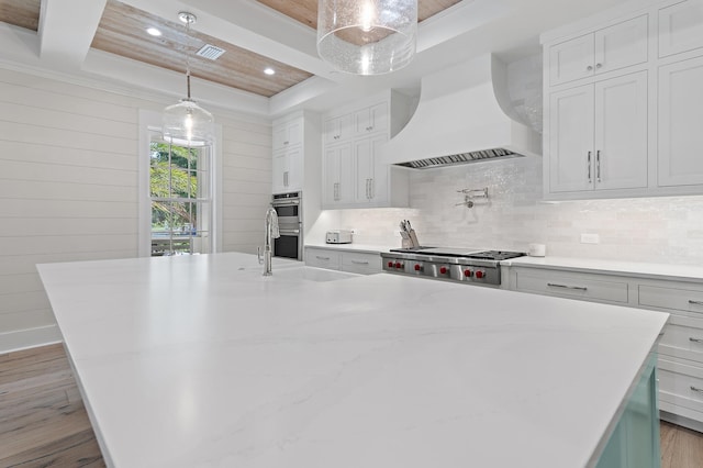 kitchen with hanging light fixtures, light hardwood / wood-style floors, white cabinetry, and custom exhaust hood