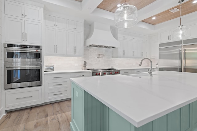 kitchen with light hardwood / wood-style floors, sink, custom exhaust hood, stainless steel appliances, and decorative light fixtures