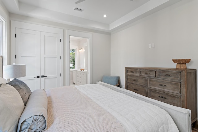 bedroom featuring connected bathroom, a tray ceiling, and a closet