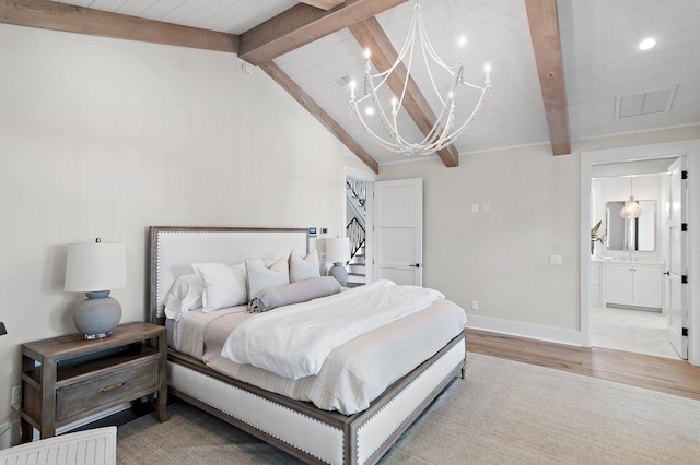 bedroom featuring lofted ceiling with beams, ensuite bath, light hardwood / wood-style floors, and an inviting chandelier