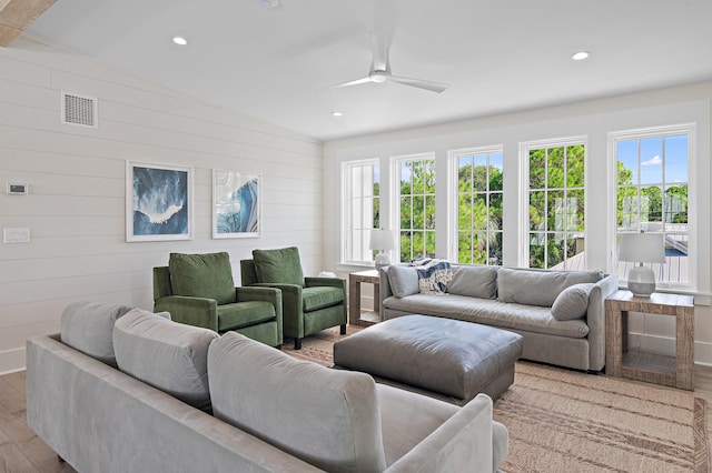 living room featuring wood walls, light hardwood / wood-style floors, vaulted ceiling, and ceiling fan