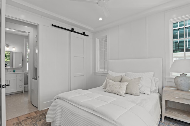 bedroom featuring ceiling fan, ensuite bathroom, hardwood / wood-style floors, and a barn door