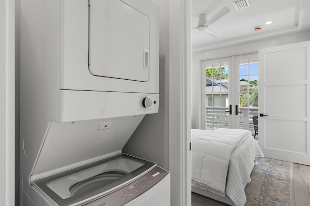 clothes washing area featuring hardwood / wood-style floors, ceiling fan, stacked washer / dryer, and french doors