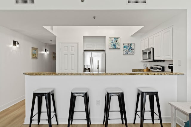 kitchen with appliances with stainless steel finishes, white cabinetry, a breakfast bar area, and light hardwood / wood-style flooring