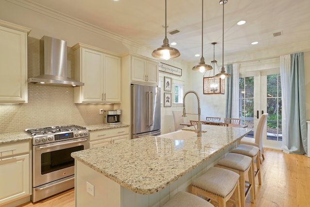 kitchen with sink, high end appliances, wall chimney range hood, and an island with sink