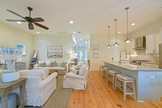 living room with light hardwood / wood-style flooring, ceiling fan, ornamental molding, and sink