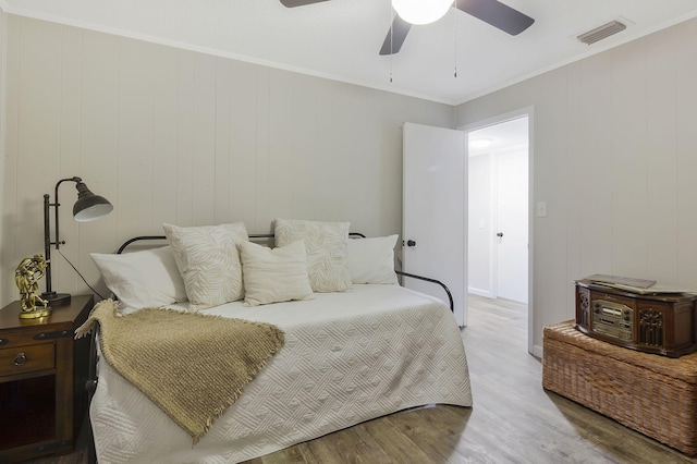 bedroom with ceiling fan, wood walls, ornamental molding, and light wood-type flooring