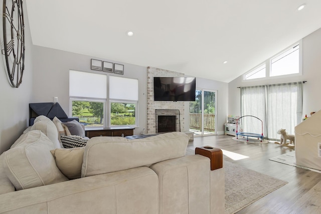 living room with high vaulted ceiling, a stone fireplace, light wood-type flooring, and a healthy amount of sunlight