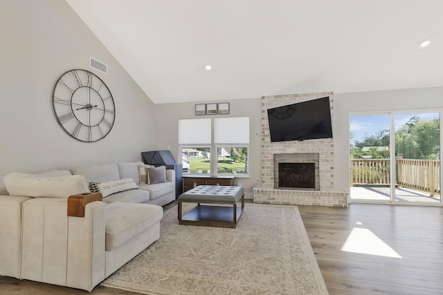 living room with light hardwood / wood-style floors, high vaulted ceiling, plenty of natural light, and a brick fireplace