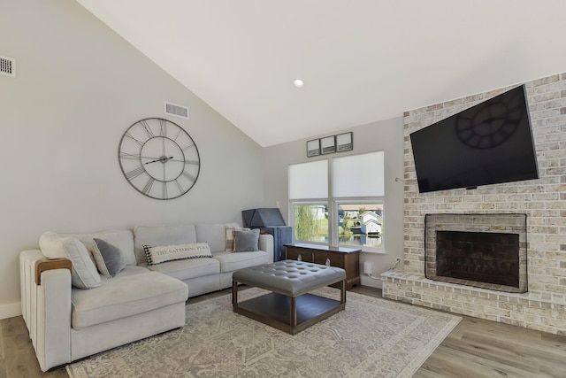 living room featuring a brick fireplace, high vaulted ceiling, and light hardwood / wood-style floors