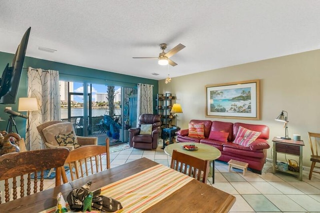 living room with a textured ceiling, light tile patterned floors, a water view, and ceiling fan