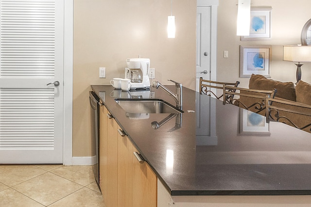 kitchen featuring light brown cabinets, light tile patterned flooring, sink, stainless steel dishwasher, and decorative light fixtures