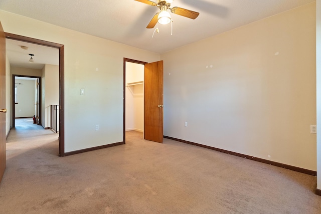 unfurnished bedroom with a walk in closet, ceiling fan, a closet, and light carpet