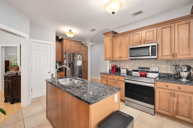 kitchen with light tile patterned flooring, a kitchen island with sink, sink, backsplash, and appliances with stainless steel finishes