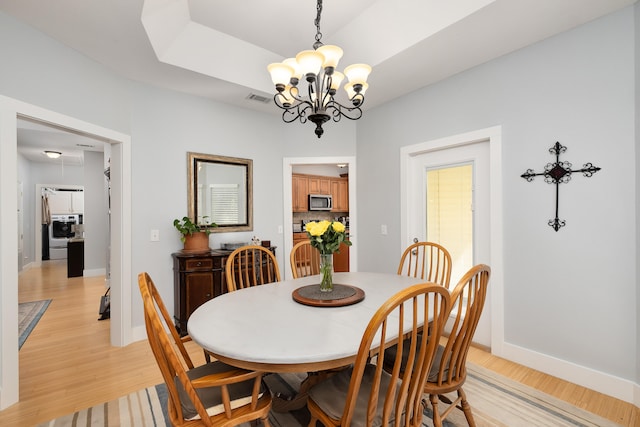 dining space with light wood-type flooring, a raised ceiling, and a chandelier