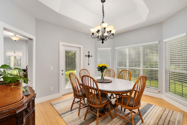 dining area featuring light hardwood / wood-style flooring, a wealth of natural light, a tray ceiling, and a notable chandelier