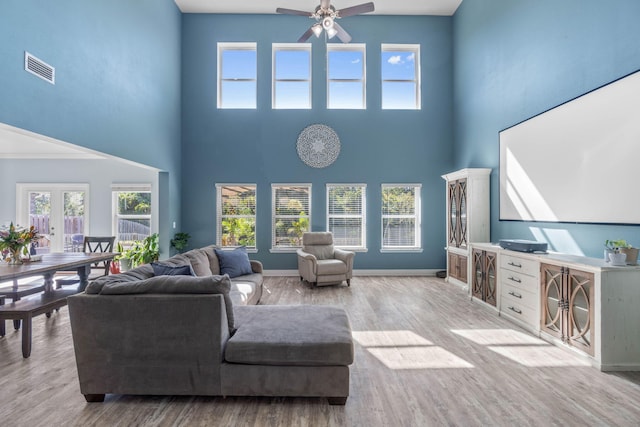 living room with a towering ceiling, light hardwood / wood-style flooring, a healthy amount of sunlight, and ceiling fan