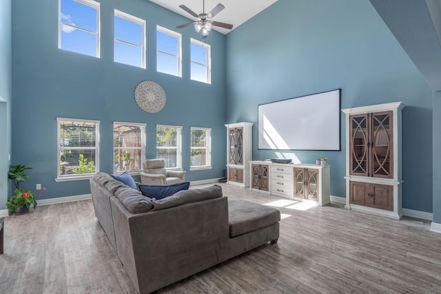 living room with a towering ceiling, hardwood / wood-style floors, a healthy amount of sunlight, and ceiling fan