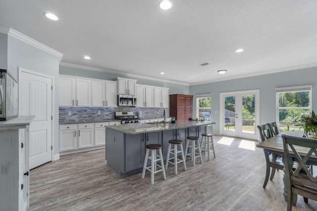 kitchen featuring a center island with sink, white cabinetry, a kitchen bar, light hardwood / wood-style floors, and stainless steel appliances