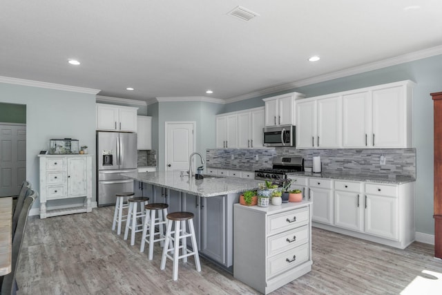 kitchen with sink, white cabinetry, light hardwood / wood-style floors, stainless steel appliances, and a kitchen island with sink