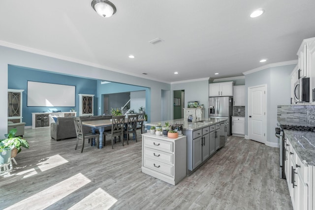 kitchen with white cabinetry, appliances with stainless steel finishes, light hardwood / wood-style flooring, and a kitchen island with sink