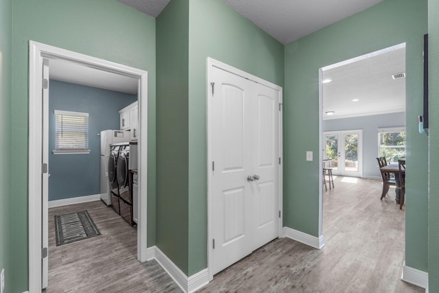 hallway with french doors, light hardwood / wood-style floors, a textured ceiling, and washer and dryer