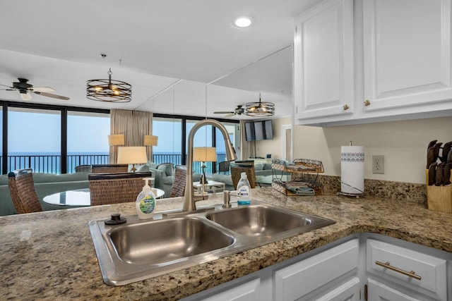 kitchen featuring a water view, ceiling fan, sink, and white cabinets