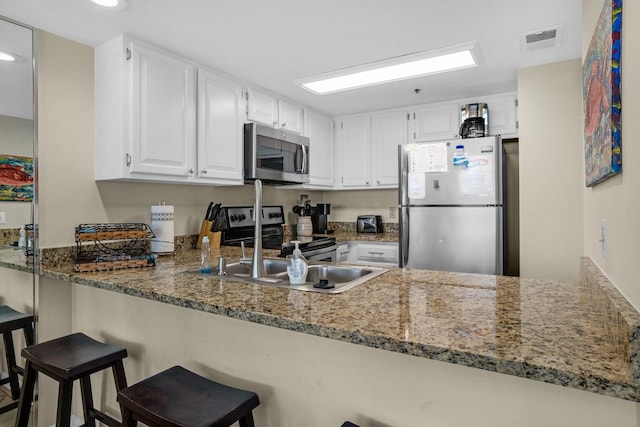 kitchen featuring kitchen peninsula, white cabinetry, light stone countertops, and appliances with stainless steel finishes