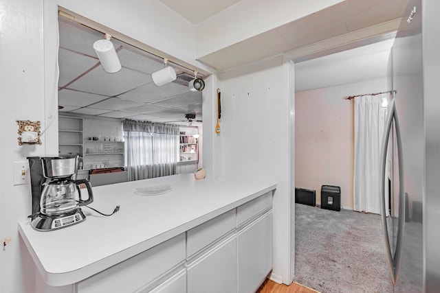 kitchen featuring light colored carpet, kitchen peninsula, ceiling fan, stainless steel refrigerator, and white cabinetry