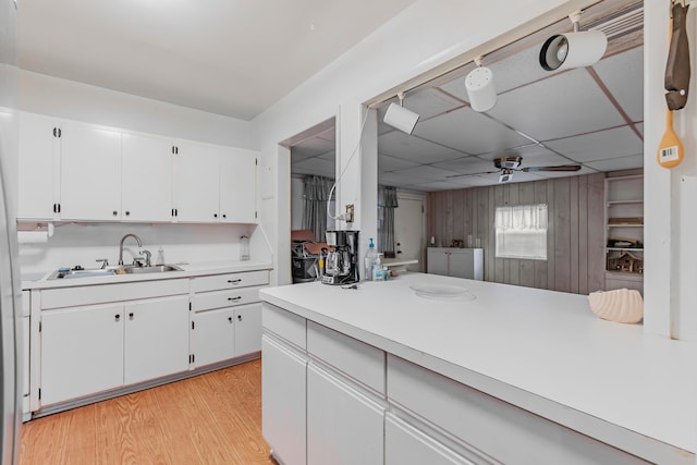 kitchen featuring sink, light hardwood / wood-style floors, white cabinets, a drop ceiling, and ceiling fan