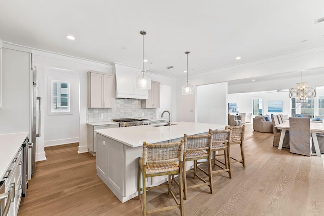 kitchen featuring white cabinets, pendant lighting, light hardwood / wood-style flooring, a kitchen island with sink, and stainless steel range