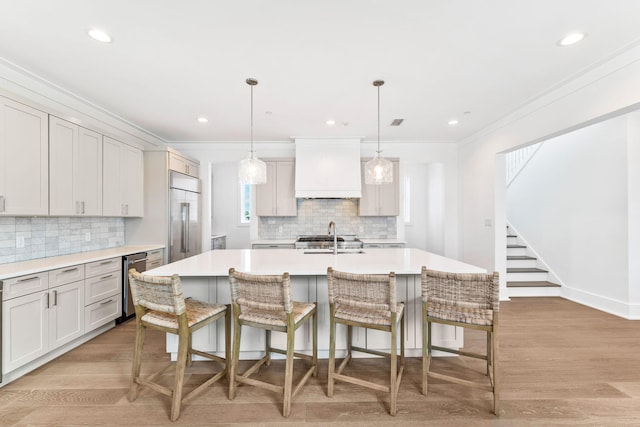 kitchen featuring built in refrigerator, a center island with sink, light hardwood / wood-style flooring, and custom range hood