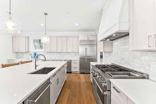 kitchen featuring custom range hood, white cabinets, high end appliances, decorative light fixtures, and sink