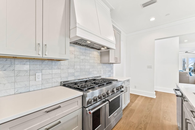 kitchen featuring double oven range, light hardwood / wood-style floors, ornamental molding, and custom exhaust hood