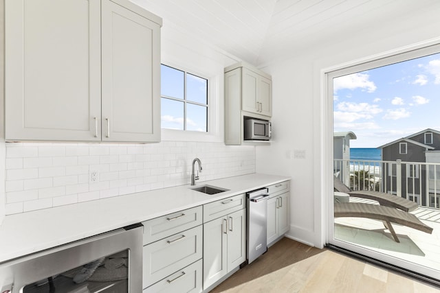 kitchen featuring sink, beverage cooler, a water view, appliances with stainless steel finishes, and hardwood / wood-style floors