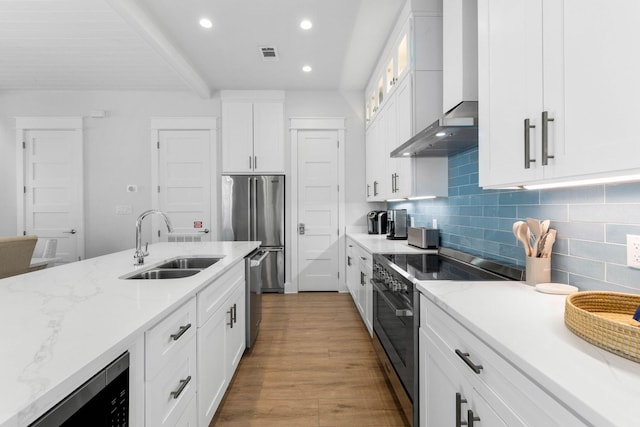 kitchen featuring sink, wall chimney exhaust hood, white cabinetry, appliances with stainless steel finishes, and light hardwood / wood-style floors