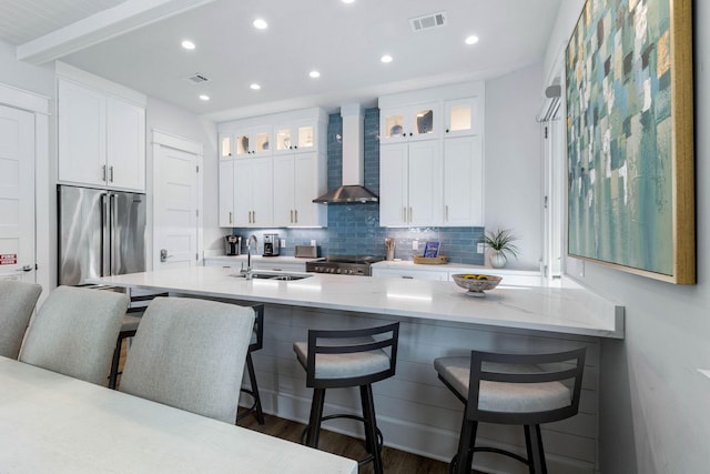 kitchen with sink, a breakfast bar area, white cabinetry, wall chimney exhaust hood, and appliances with stainless steel finishes