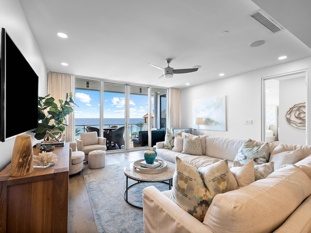 living room featuring a wall of windows, hardwood / wood-style floors, a water view, and ceiling fan