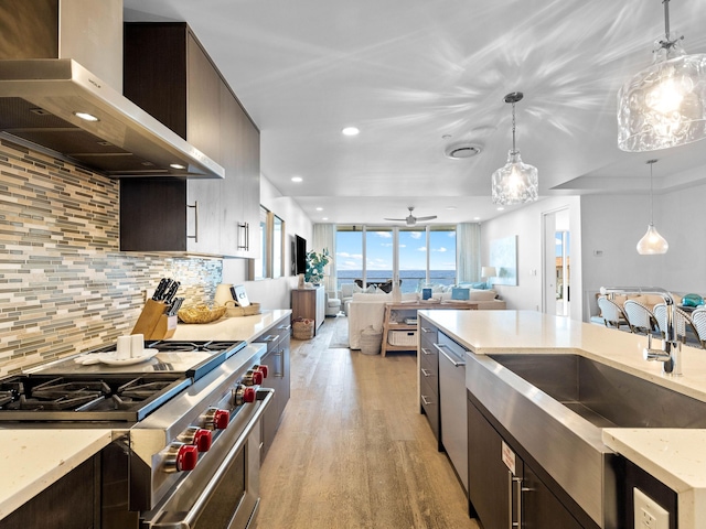 kitchen featuring wall chimney range hood, stainless steel appliances, pendant lighting, light wood-type flooring, and tasteful backsplash