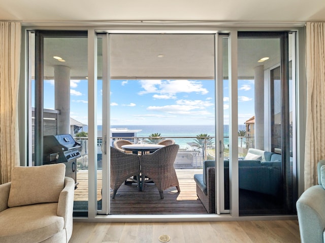 doorway to outside with light wood-type flooring, a wall of windows, a water view, and a healthy amount of sunlight