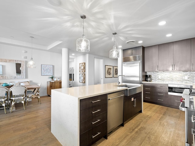 kitchen featuring appliances with stainless steel finishes, light hardwood / wood-style flooring, an island with sink, and pendant lighting