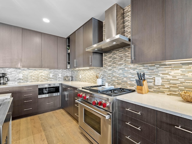 kitchen with decorative backsplash, wall chimney range hood, luxury range, dark brown cabinetry, and light hardwood / wood-style floors