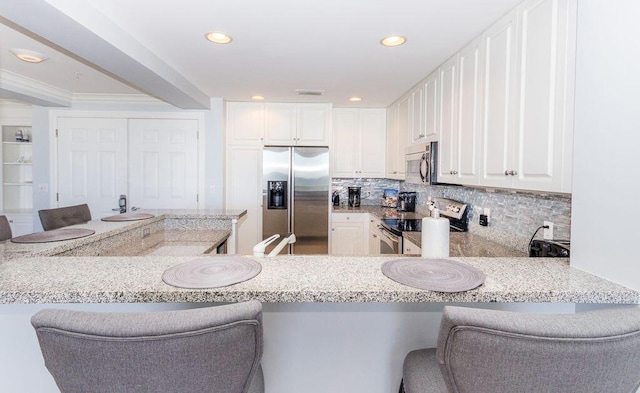 kitchen with a breakfast bar, stainless steel appliances, white cabinets, and kitchen peninsula