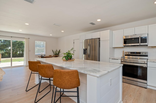 kitchen with light hardwood / wood-style floors, appliances with stainless steel finishes, a kitchen island, and white cabinets