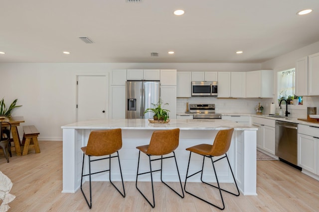 kitchen featuring appliances with stainless steel finishes, white cabinets, a center island, and light wood-type flooring