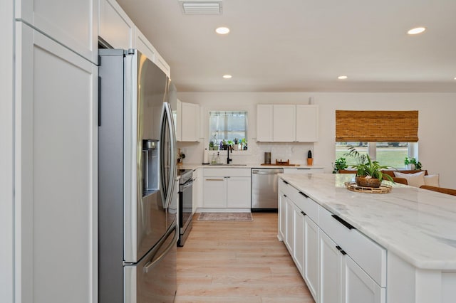 kitchen featuring appliances with stainless steel finishes, light hardwood / wood-style flooring, white cabinets, and light stone counters