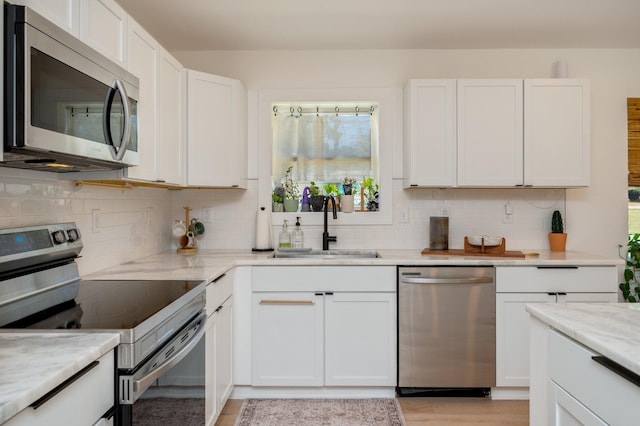 kitchen with light stone countertops, sink, light wood-type flooring, white cabinetry, and stainless steel appliances